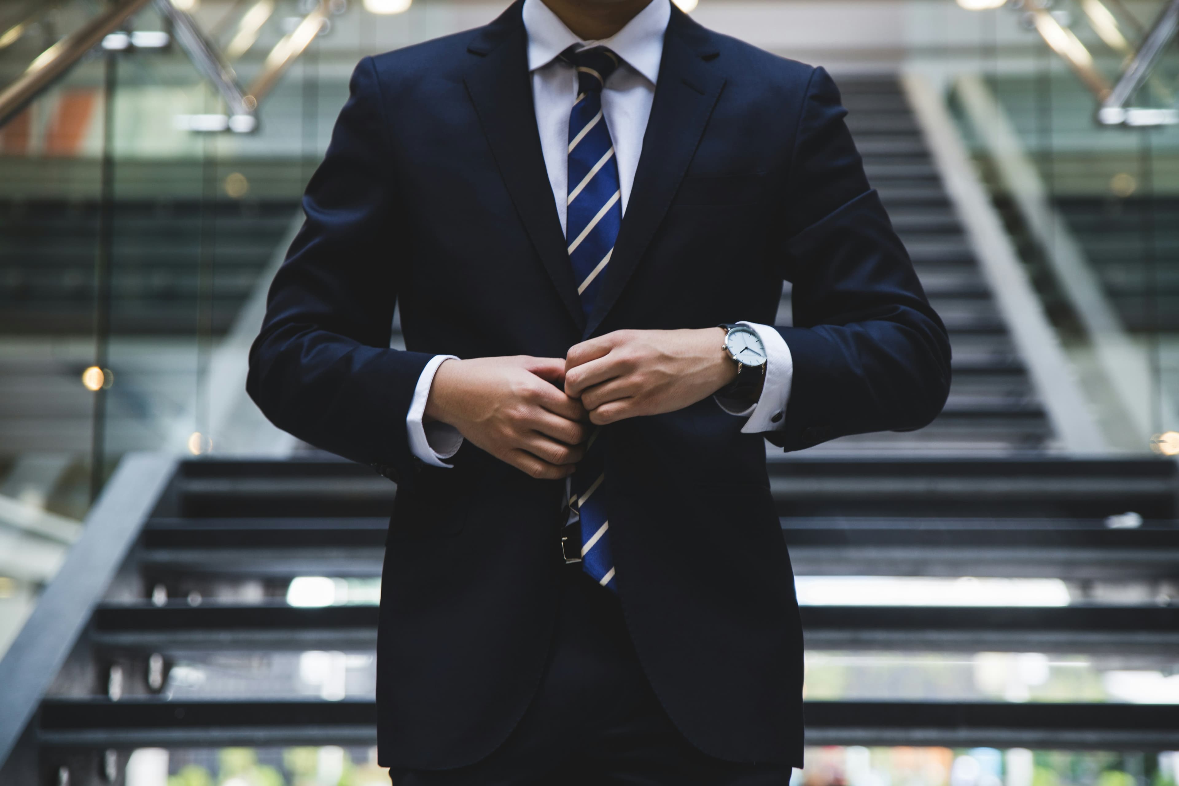 A person in a navy suit fastening their jacket button at the foot of an office staircase